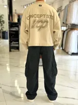 Buzo oversize color beige, con costuras externas visibles y gran estampado tipográfico y gráfico en la espalda.