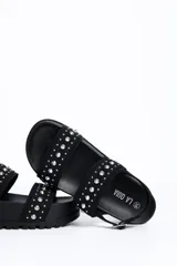 Sandalia chunky de plataforma color negro, con diseño de doble tira ancha decorada con tachas metálicas cónicas y pulsera ajustable al tobillo con hebilla.