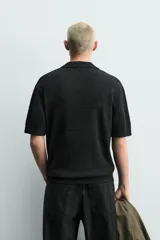 Polo de punto color negro con textura irregular, cuello solapa con abertura frontal, manga corta y acabados en rib, de corte relaxed fit.
