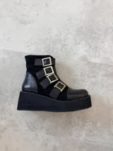 Botas cortas de cuero negro con plataforma y cuatro hebillas metálicas laterales.