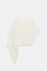Camiseta tipo capa oversize de color blanco, confeccionada en hilatura de algodón 100%. Presenta cuello redondo, manga corta y un diseño de bajo asimétrico con caída pronunciada en uno de los laterales.