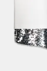 Camiseta negra de corte oversize, cuello redondo y manga corta. Presenta un bajo asimétrico con una aplicación de lentejuelas plateadas a contraste.