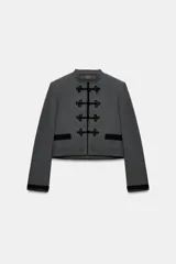 Blazer de corte cropped confeccionado en tejido de lana gris, con cuello redondo y cierre frontal mediante alamares decorativos. Presenta bolsillos delanteros con solapa y puños a contraste en color negro.