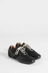 Zapatillas negras de estilo urbano con cordones blancos, confeccionadas en cuero sintético y poliéster, con diseño de paneles y suela plana.