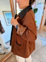 Campera de ecocuero color chocolate, con diseño amplio y relajado. Presenta cuello camisero, cierre frontal con cremallera y botones a presión, además de bolsillos delanteros amplios.
