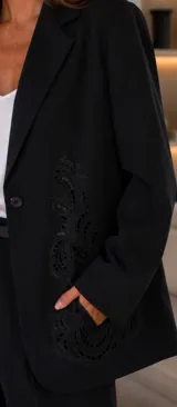 Blazer negro de corte clásico con cierre frontal de un botón y detalle de bordado ornamental a tono en el lateral. Posee un largo a la cadera.
