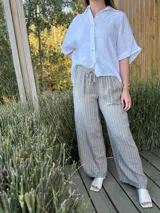 Pantalón de corte ancho y relajado, confeccionado en lino con diseño de rayas verticales. Presenta cintura elástica con cordón de ajuste y bolsillos laterales.