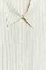 Camisa oversize de popelina con estampado de rayas verticales en tonos blanco y amarillo, cuello de solapa, manga corta con vuelta y cierre frontal de botones.