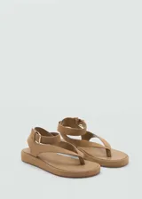 Sandalias planas de tipo dedo o thong, color marrón tostado, confeccionadas en piel bovino con acabado de gamuza. Tienen diseño de tiras anchas, puntera redonda y tira al tobillo con hebilla metálica dorada.