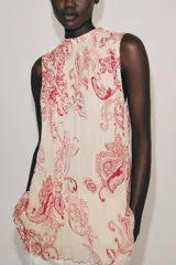 Top sin mangas confeccionado en hilatura de viscosa, con cuello redondo y cierre en la espalda con abertura y botón. Presenta un diseño con estampado paisley a contraste en color rojo sobre fondo beige.