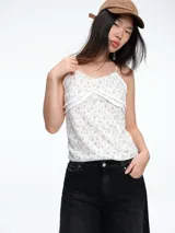 Top lencero de tirantes finos con estampado floral pequeño sobre fondo blanco. Presenta detalles de volados en el pecho y una textura acanalada sutil.