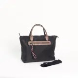 Cartera tipo tote de color negro con detalles en tono beige. Cuenta con doble asa de mano, un bolsillo frontal con cierre y un colgante decorativo de cuerda trenzada multicolor. Incluye una correa larga ajustable y extraíble.