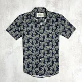 Camisa de hombre de manga corta con estampado de hojas verdes sobre fondo negro.