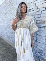 Túnica larga de estilo boho, color crudo con estampado de arabescos y detalles en hilo dorado. Presenta escote en V, mangas amplias tipo kimono y cordón ajustable en la cintura con borlas decorativas.