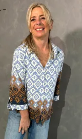 Blusa de manga larga con cuello camisero, corte recto y cierre frontal de botones. Presenta un diseño estampado geométrico en tonos celeste, blanco y marrón.