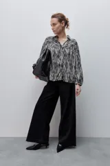 Camisa de calce amplio confeccionada en viscosa fluida con estampado animal print tipo cebra en blanco y negro. Presenta cuello camisero, escote en V y mangas largas con puños elastizados, además de frunces en el canesú que aportan volumen.