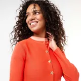 Cárdigan de punto color naranja con corte peplum, cuello redondo y cierre frontal con botones dorados en forma de estrella.