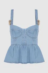 Blusa tipo corset de denim azul claro, con diseño estructurado, escote recto y volado en la cintura. Presenta breteles anchos con detalles de esferas metálicas doradas en la unión con el cuerpo.