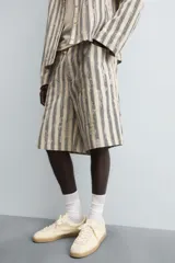 Bermuda de hombre color beige con estampado de rayas verticales azules con efecto desgastado. Corte relaxed fit, con cierre frontal de cremallera y botón, bolsillos delanteros y bolsillos traseros de plastrón.