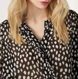Camisa de manga larga con estampado de manchas blancas sobre fondo negro, confeccionada en tejido semitransparente. Presenta cuello clásico, cierre frontal con botones ocultos y puños abotonados.