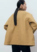 Anorak de estilo oversize en color tostado, con cuello camisero de pana en contraste. Presenta cierre frontal mediante ganchos metálicos y dos bolsillos de parche con solapa en la parte delantera.