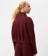 Campera de modal color marrón, con cuello alto, cierre frontal completo y diseño con pliegues en el ruedo. Presenta mangas largas y un calce holgado.