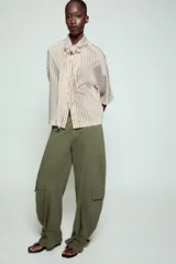Pantalón cargo de tiro medio confeccionado en algodón, con diseño de pierna ancha y costuras verticales. Presenta bolsillos laterales y bolsillos tipo cargo con solapa en las piernas. El bajo es ajustable mediante trabillas con hebilla metálica.