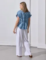 Blusa de lyocell color celeste con estampado de motivos playeros en blanco. Tiene cuello a la base con escote en V, mangas cortas con volados y detalle fruncido en mangas y espalda.