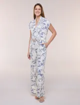 Enterito largo color blanco con estampa ilustrada en azul estilo Toile de Jouy, escote en V cruzado, mangas cortas caídas, bolsillos laterales, pantalón amplio wide leg y cinturón incorporado con hebilla metálica.