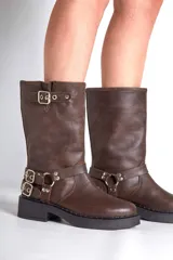 Borcego de cuero color marrón con apliques plateados, caña alta y suela track.