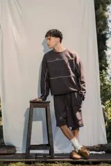 Buzo crewneck color chocolate, de tela rústica liviana, con estampado en el frente y la espalda. Presenta líneas blancas decorativas en el pecho y los brazos, y bordes deshilachados en los puños y el dobladillo.