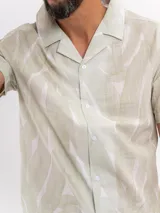 Camisa de manga corta de algodón en color beige, con cuello camisero y cierre frontal de botones, con diseño estampado sutil.