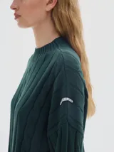 Buzo tejido de punto color beige, con cuello subido, diseño oversized y aberturas laterales en el ruedo.