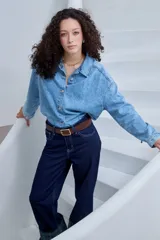 Pantalón de jean azul oscuro, de corte recto y tiro alto, con costuras a contratono y detalle de dobladillo vuelto con estampa a cuadros en tonos verdes y azules.