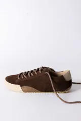 Championes urbanos de gamuza color marrón, con suela de goma en tono crema y cordones jaspeados. Presenta un refuerzo en la puntera y un detalle en cuero beige en el talón.