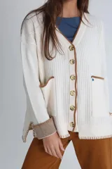 Cárdigan tejido color crudo con cuello en V, cierre con botones y bolsillos frontales con ribete en marrón.