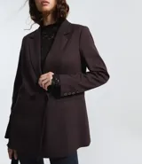 Blazer de sastrería en color negro, de corte alargado y estructura recta. Presenta solapas clásicas, cierre frontal con dos botones, hombros estructurados y mangas largas con detalle de botones en los puños. Incluye bolsillos decorativos y forro interno.