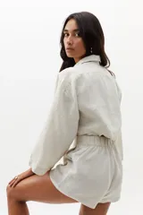 Short de lino color natural, de cintura alta con elástico en la parte trasera, ruedo curvo, bolsillos laterales y cierre frontal escondido.