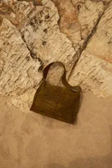 Cartera de hombro tipo hobo, confeccionada en cuero con textura de reptil. Presenta un diseño estructurado con costuras visibles y cierre superior.