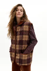 Chaleco acolchado de corte holgado con estampado de cuadros en tonos marrones y burdeos. Presenta cuello y ribetes en pana color caramelo, cierre frontal con botones a presión ocultos y bolsillos de parche delanteros.