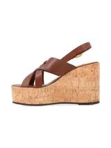 Sandalias de plataforma con taco acuñado de corcho y tiras cruzadas de cuero marrón en el empeine, con tira ajustable al talón y hebilla metálica dorada.