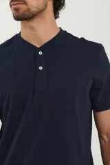 Remera tipo henley de manga corta, color beige, con cuello redondo y cartera de botones frontal.