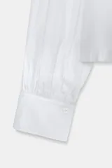 Camisa de popelín color verde militar, con cuello solapa, mangas largas abullonadas terminadas en puño, bajo recto y cierre frontal con botones ocultos por solapa.