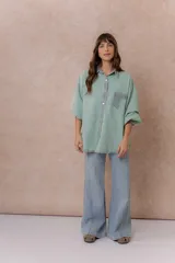 Camisa de denim color verde menta con calce relajado, cuello clásico, cierre frontal con broches metálicos, mangas largas y bolsillo aplicado en el pecho, con detalles en tono gris azulado a contraste en cuello, cartera, bolsillo y puños.