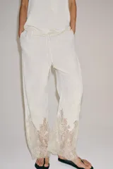 Pantalón de tiro medio con cintura elástica ajustable mediante cordones. Presenta un diseño fluido con bolsillos laterales ocultos y bajo decorado con una aplicación de encaje a contraste.