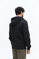 Campera de felpa color camel con cierre frontal, capucha ajustable con cordones negros y bolsillos laterales con cierre negro. Presenta un estampado pequeño en el pecho con texto en color oscuro.