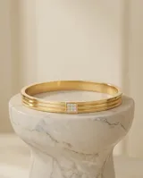 Pulsera tipo esclava rígida de acero con baño de oro, compuesta por tres bandas paralelas y un detalle central cuadrado adornado con circonias.