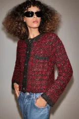 Chaqueta de punto con textura y estructura de tweed, en combinación de rojo y negro. Cuenta con cuello redondo, manga larga, bolsillos delanteros de plastrón y cierre frontal con botones metálicos dorados.