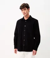 Camisa de terciopelo cotelé color negro, de corte clásico con cuello solapa, manga larga, cierre frontal de botones y un bolsillo aplicado en el pecho.