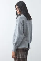 Polera de tejido de punto color gris, con cuello alto, mangas largas abullonadas con puños elásticos y costura central vertical en el frente. Presenta una abertura sutil en la espalda.